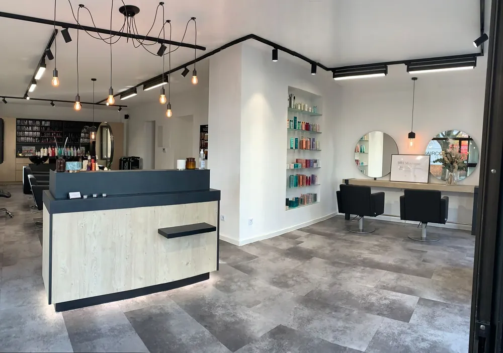 Der Salon von Hairconcept by Tuğba in Nürnberg: Empfang, Bedieninsel, runde Spiegel und Regale mit Pflegeprodukten unter warmem Licht